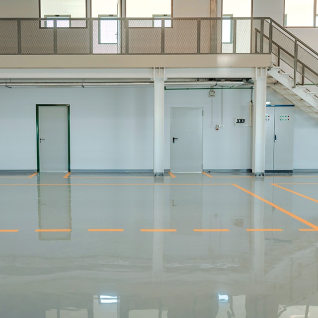 An indoor facility with off-white painted walls, a gray floor with orange-painted lines and dashes, and stairs leading to second-story rooms with open doors.