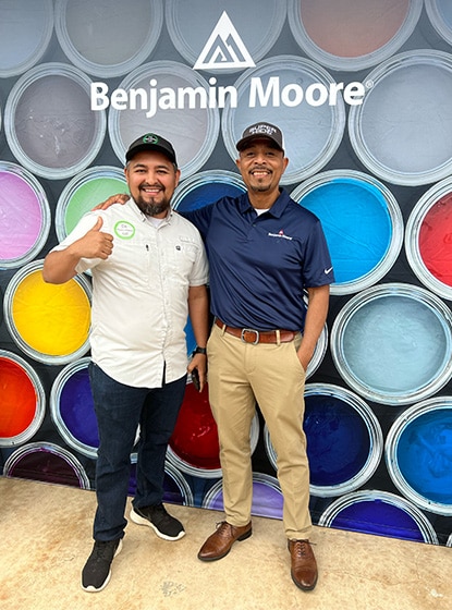 Deux hommes posant devant une toile de fond Benjamin Moore arborant des contenants de peinture ouverts et colorés.